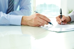 Two people signing estate planning documents in a business setting.
